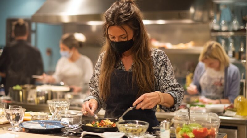 Woman in an apron and mask preparing food during a cooking class with others in the background