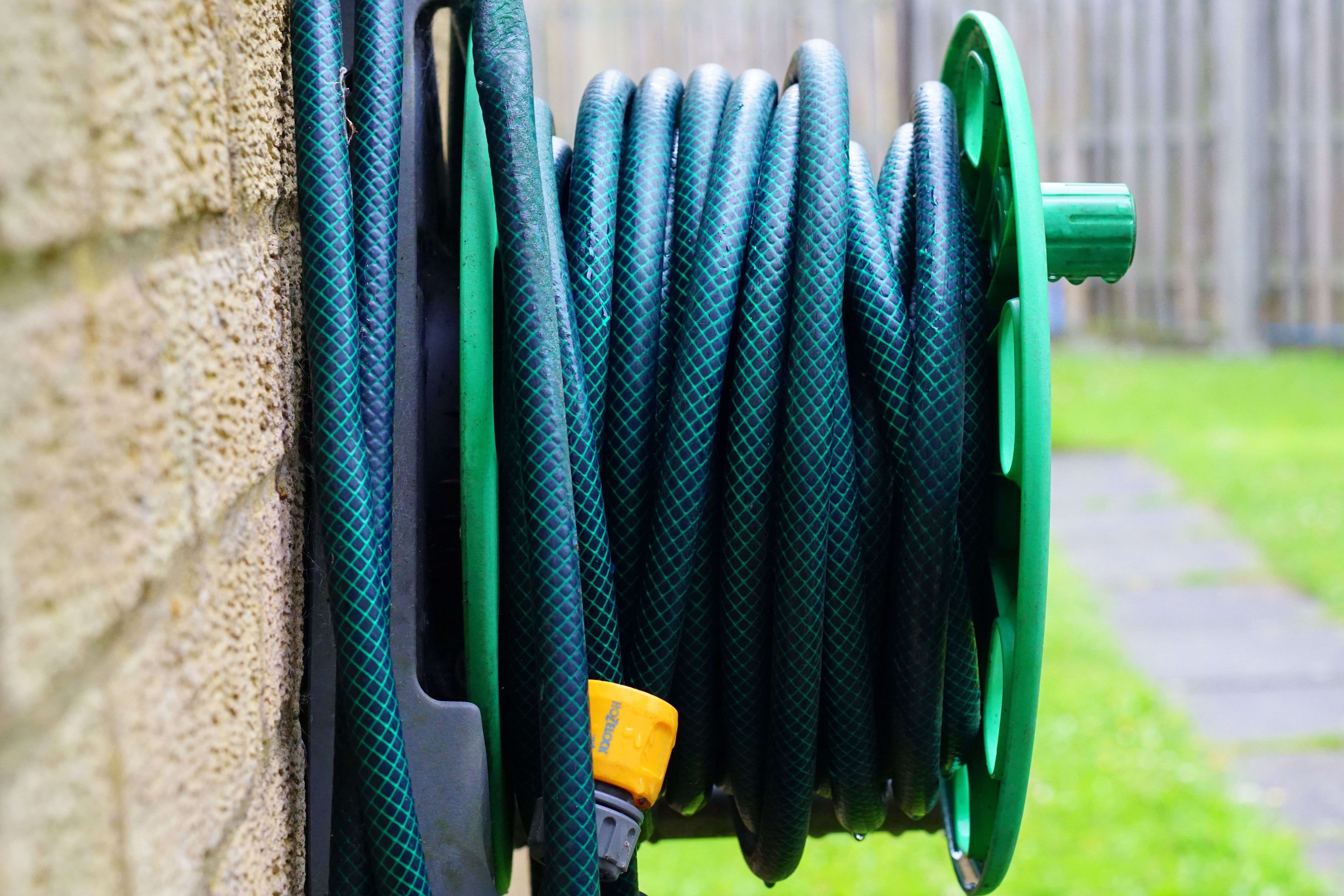 Coiled garden hose on a wall-mounted reel beside a brick wall, showing a practical long-lasting backyard improvement.